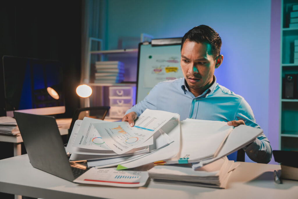 Employé de bureau submergé par les tâches et les dossiers devant son écran d'ordinateur.