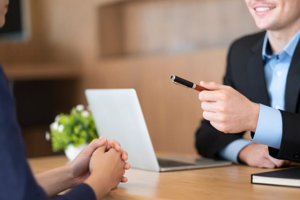 Un recruteur tendant un stylo à un candidat lors d'un test de vente en direct.