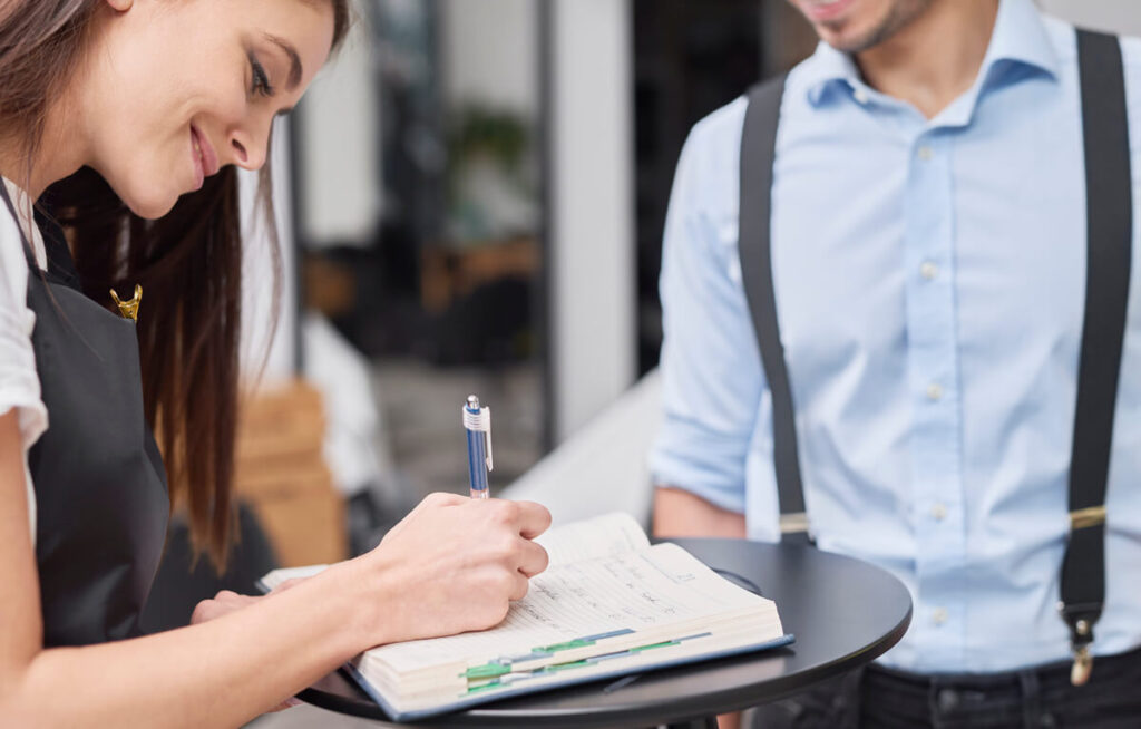 Jeune serveur en tenue passant un test de compétence en salle de restaurant sous l'œil du gérant