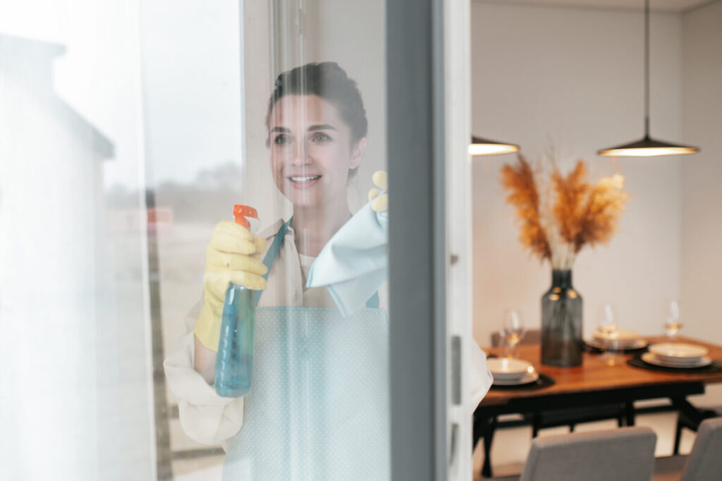 Une employée de maison effectuant le nettoyage des vitres dans le salon lumineux d'une maison de vacances. Une employée de maison effectuant le nettoyage des vitres dans le salon lumineux d'une maison de vacances.