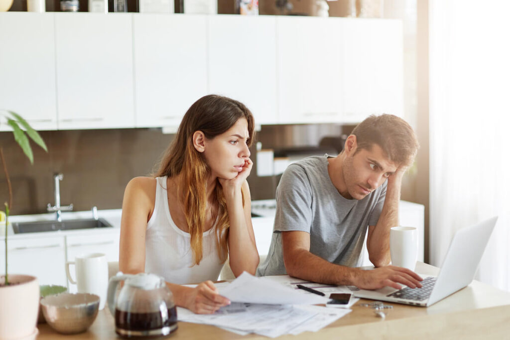 Un couple assis à table au milieu de factures et de comptes bancaires, illustrant les tensions financières.