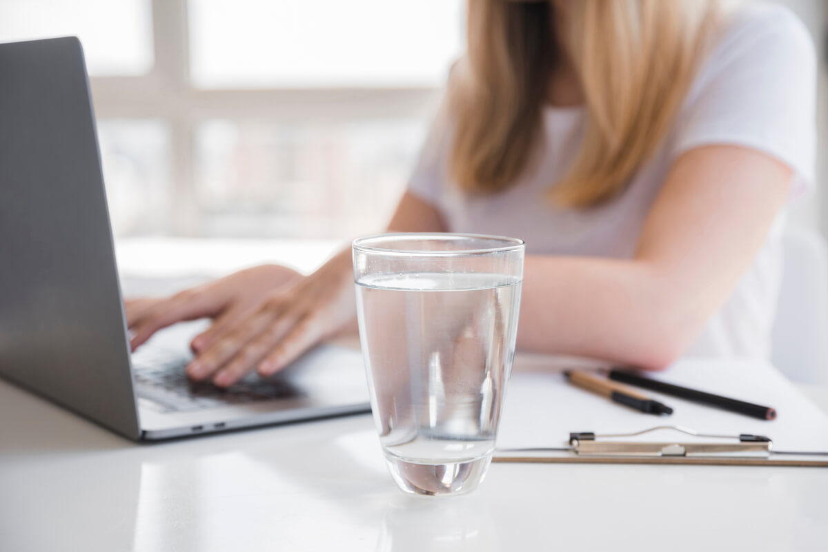 Une personne vérifiant sa facture d'eau avec un verre d'eau posé à côté sur la table.