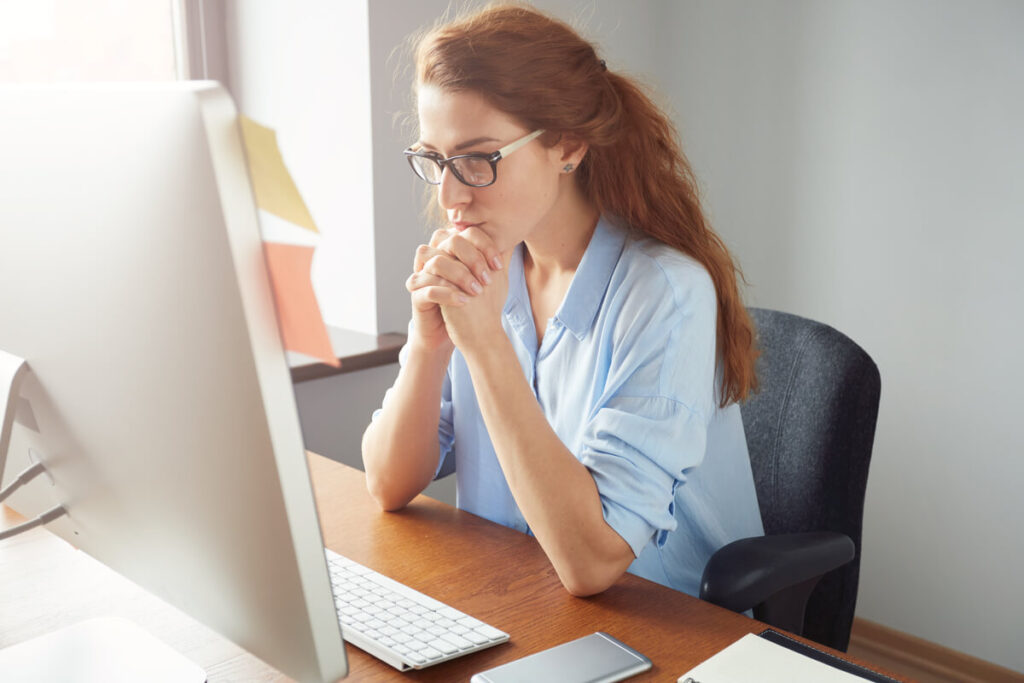 Une femme d'une quarantaine d'années pensive devant son écran d'ordinateur au bureau, le menton appuyé sur la main.