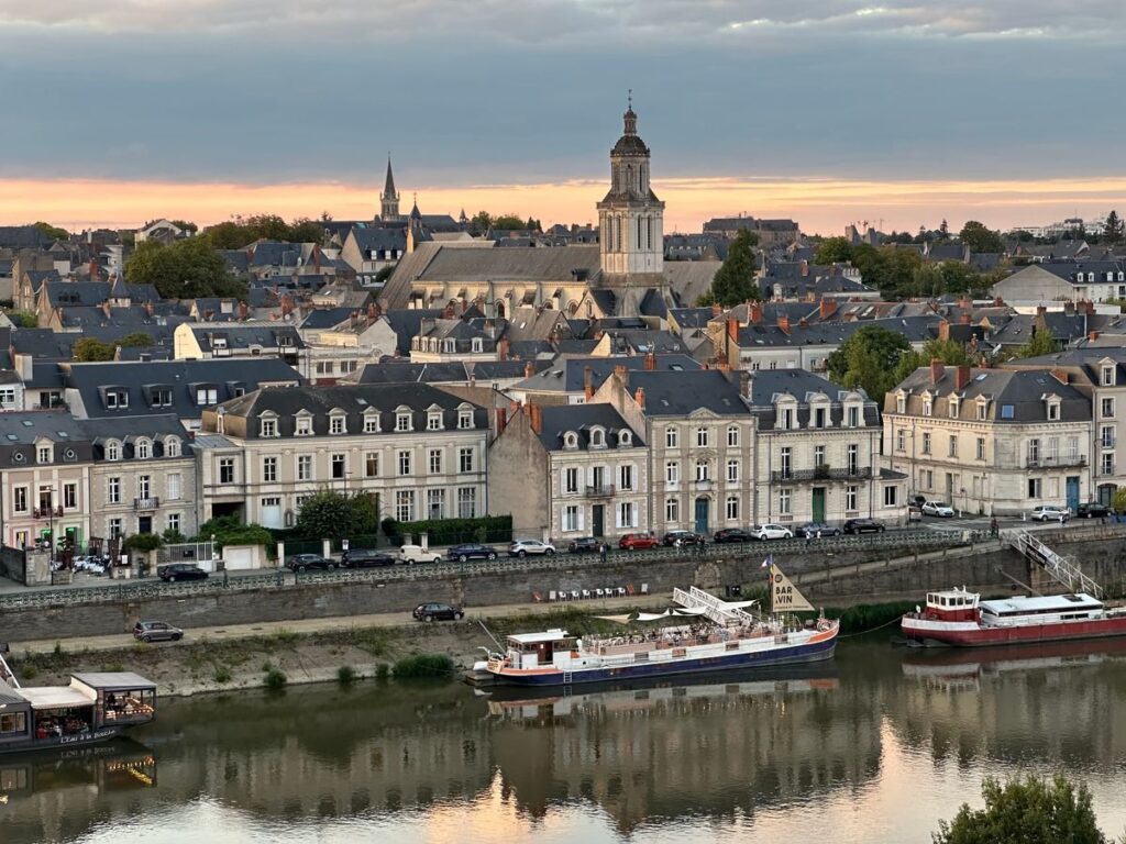 Vue de la ville d'Angers au coucher du soleil avec ses immeubles anciens, ses clochers et des péniches amarrées le long de la rivière